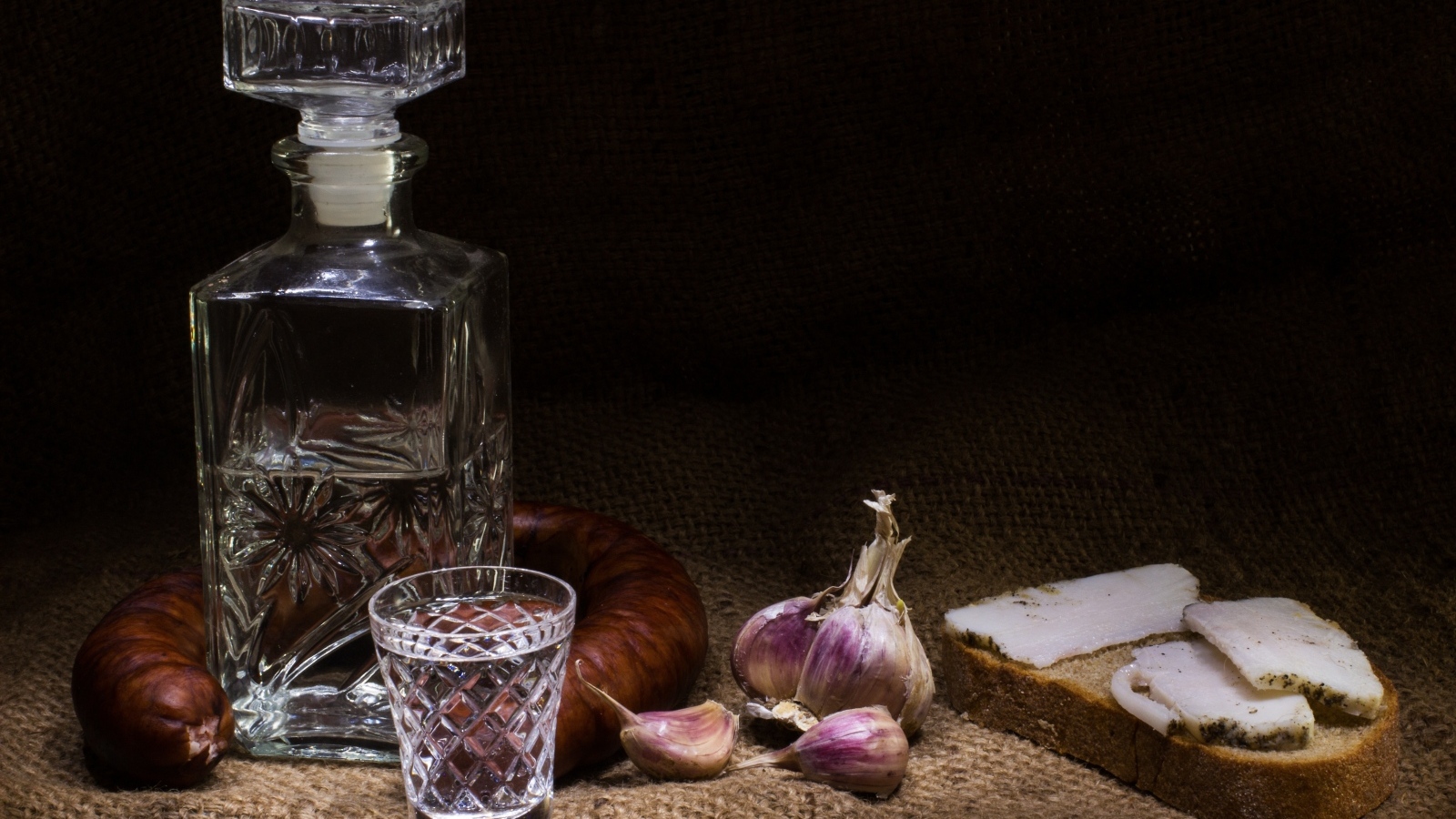 Бутылка водки на столе с салом, колбасой и чесноком