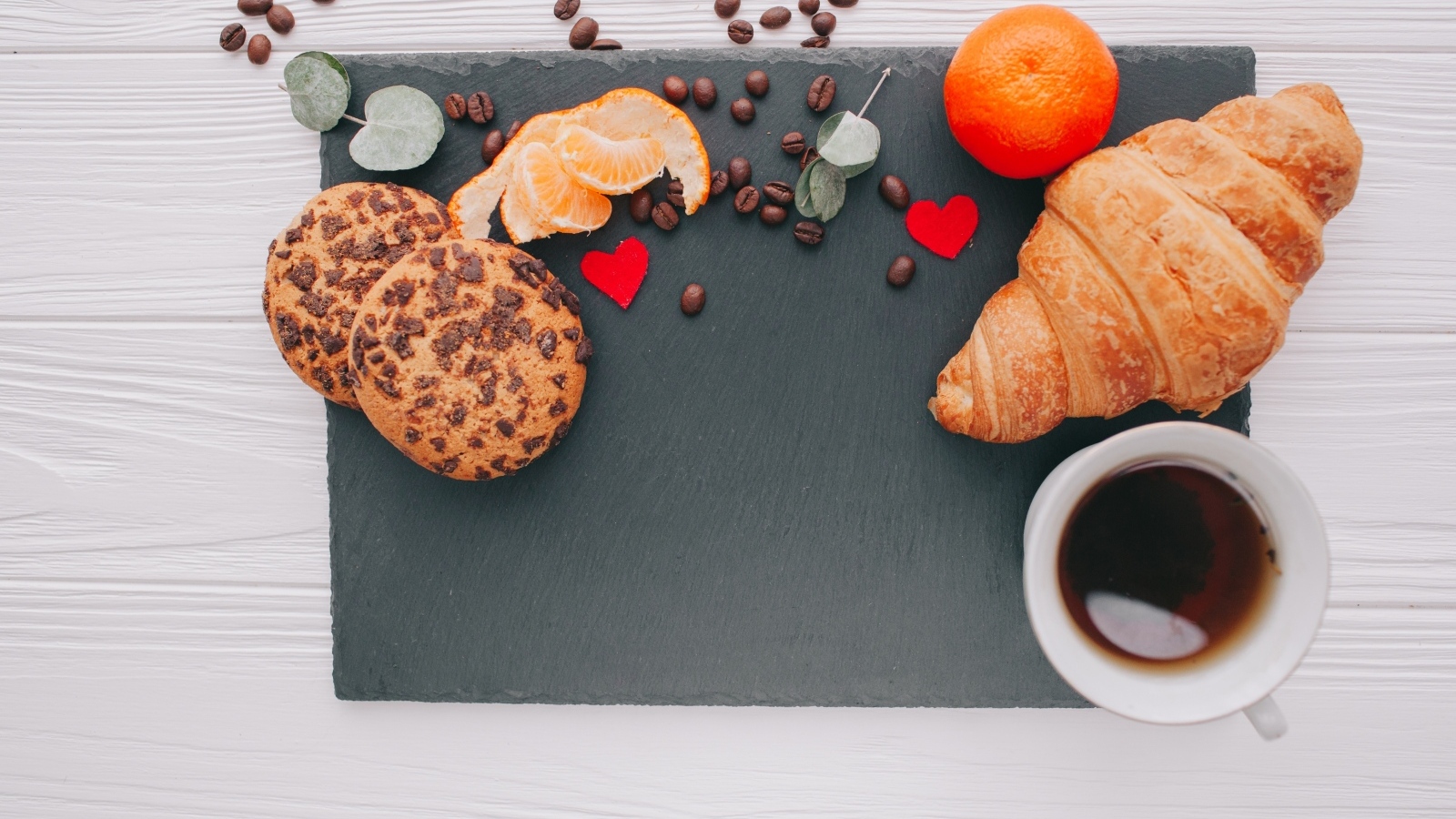 Круассан на столе с печенье, чашкой кофе и мандарином