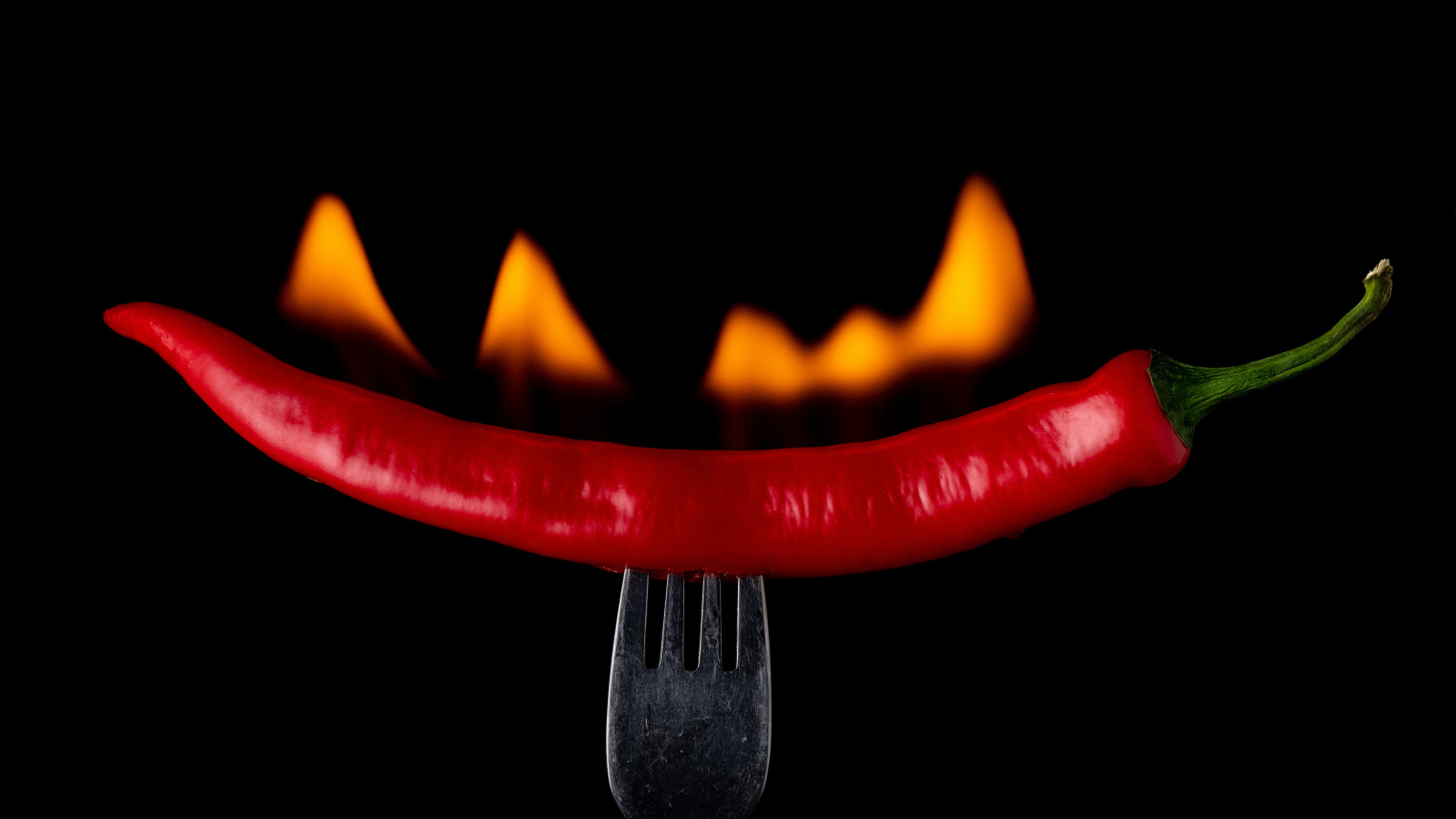 Жгучий красный перец на вилке на черном фоне