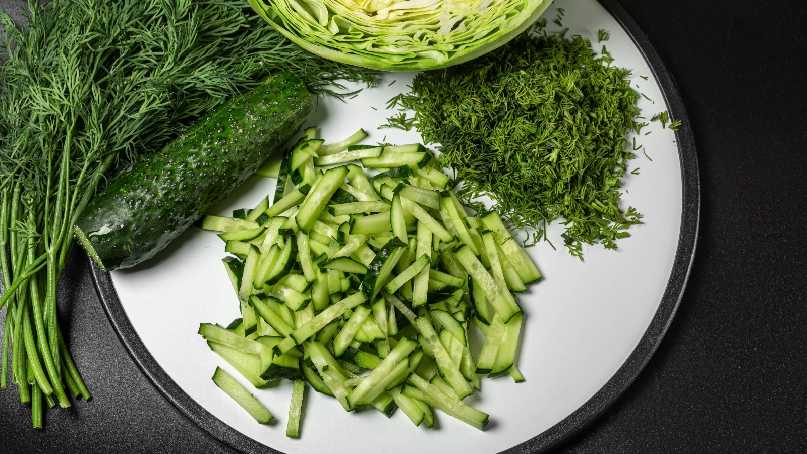 Нарезанные огурцы на столе с капустой и укропом