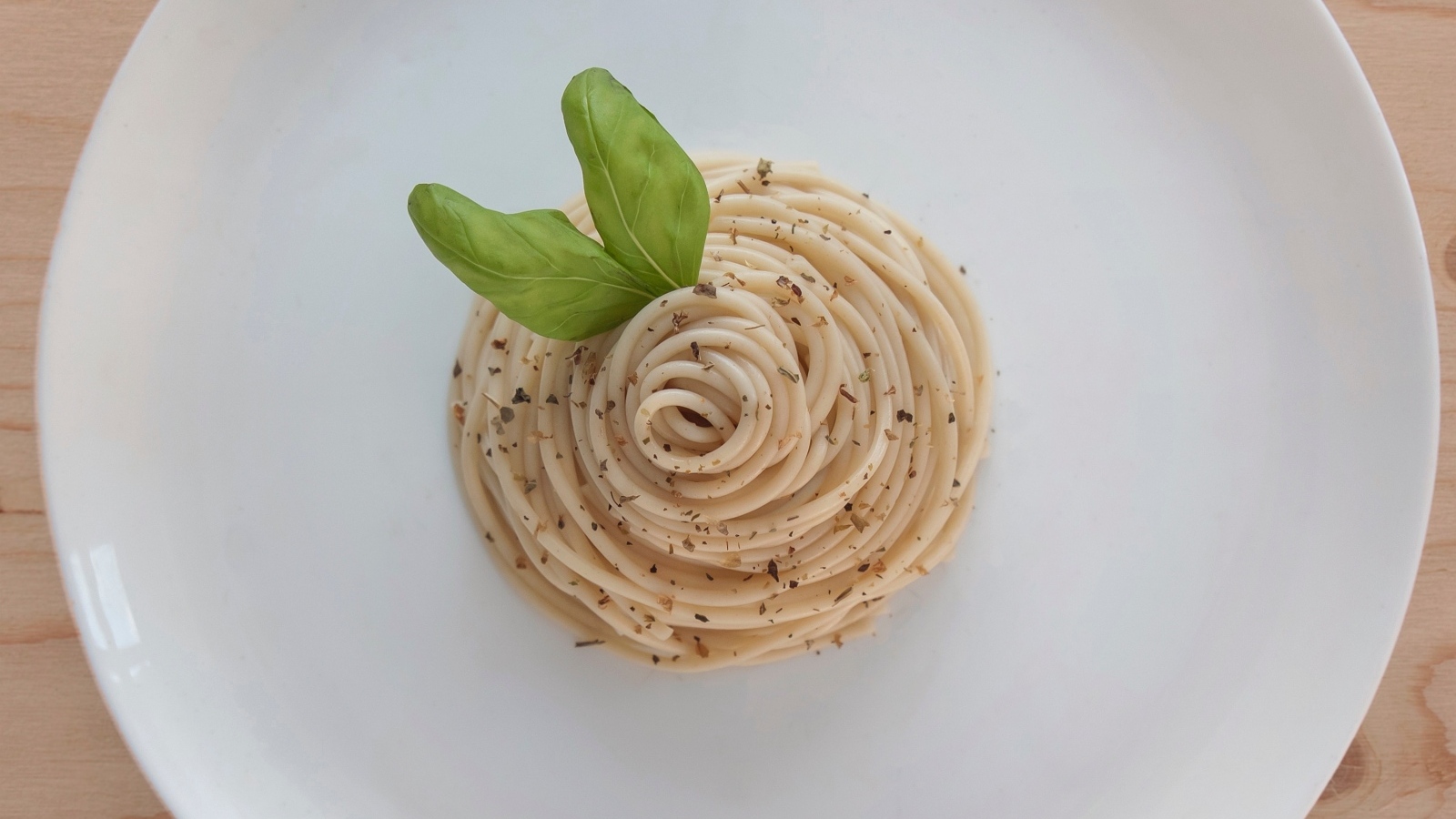 Спагетти с листьями базилика на белой тарелке