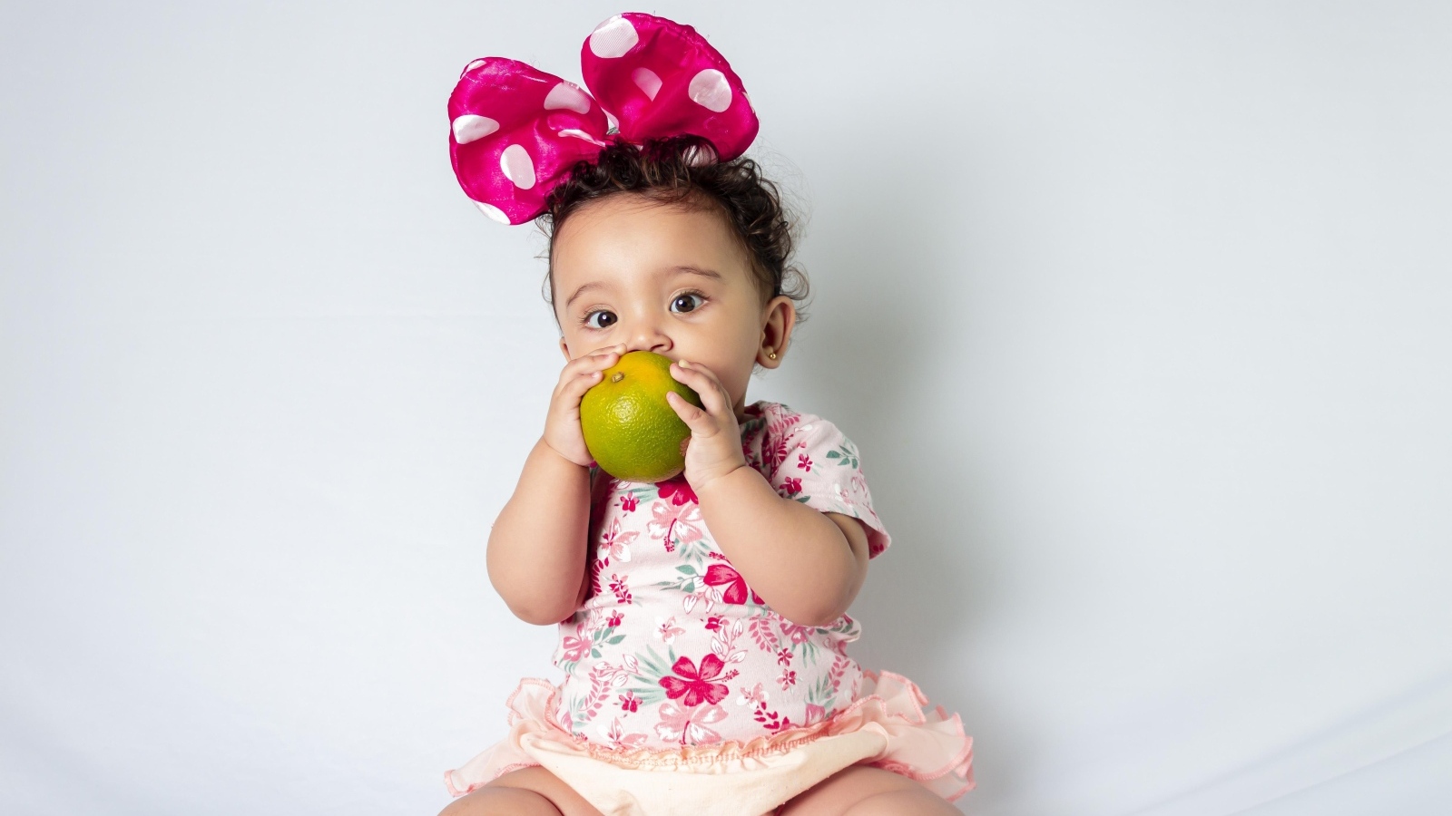 Девочка с большим бантом на голове ест апельсин