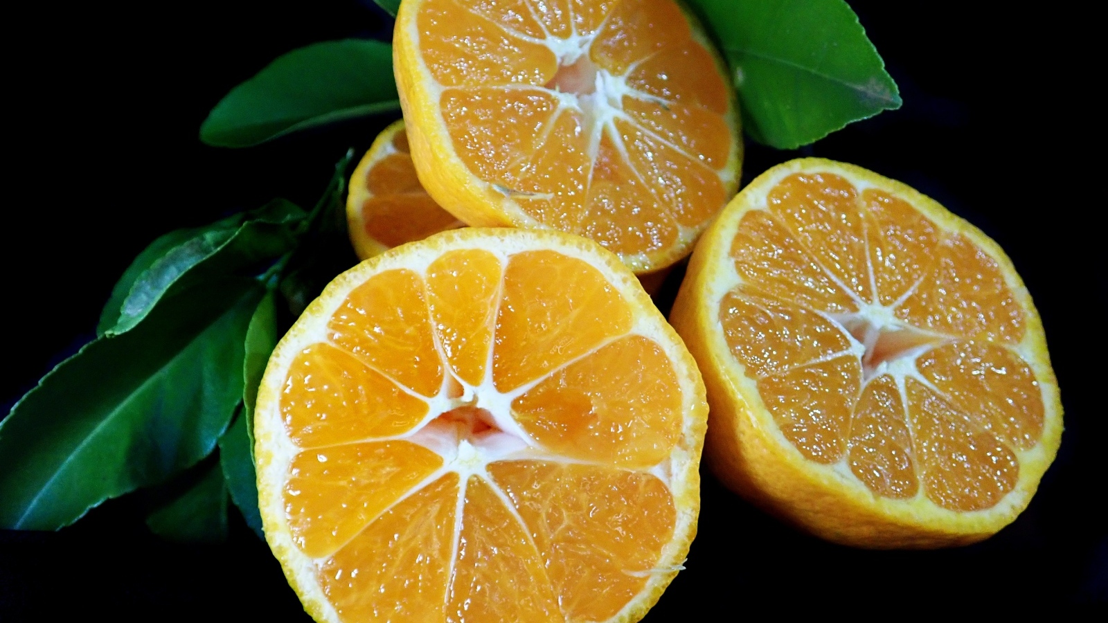Половинки мандарина с зелеными листьями на черном фоне