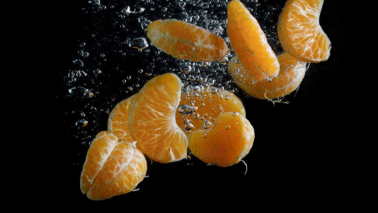 Дольки мандарина в воде на черном фоне