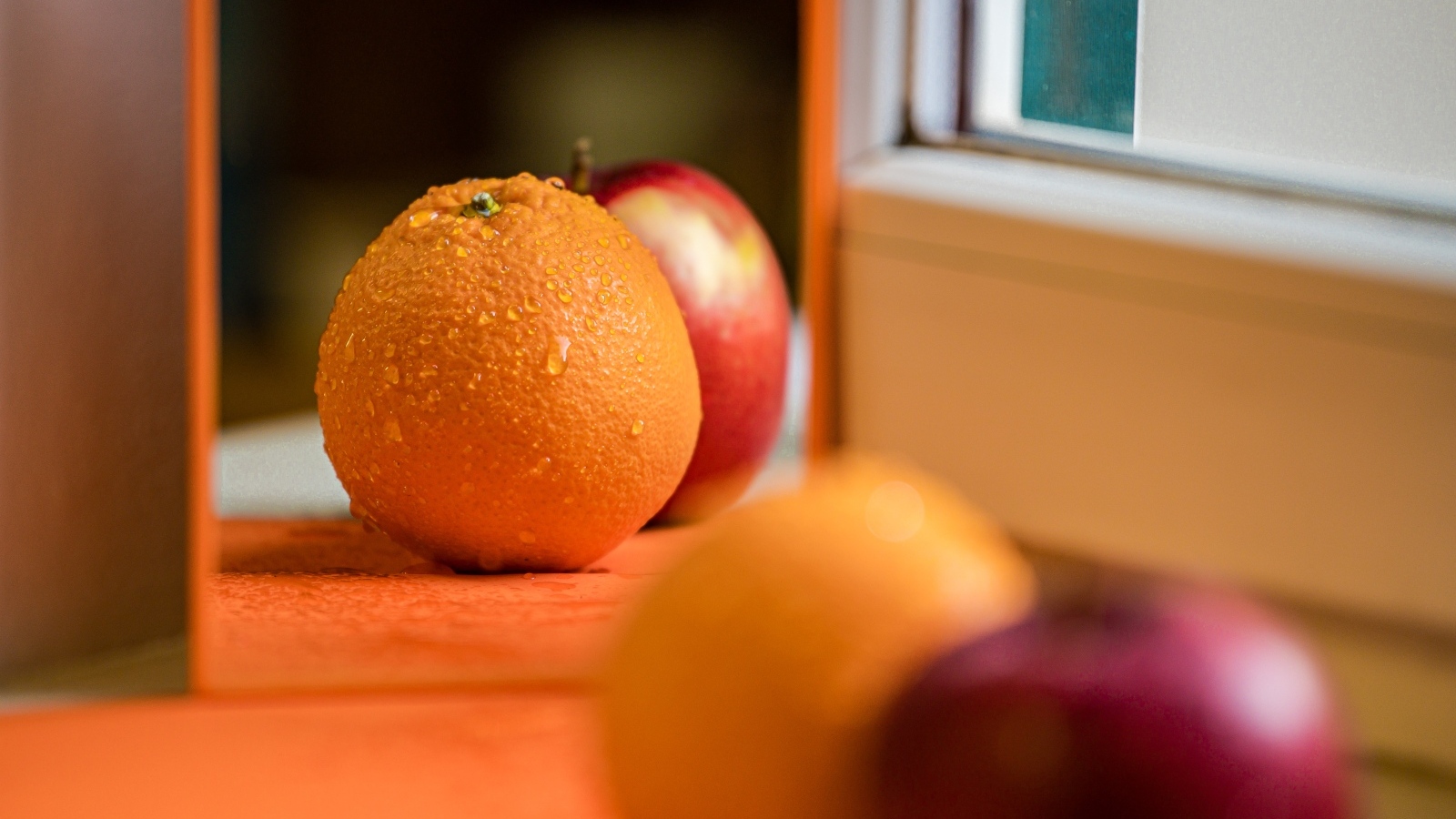 Апельсин и яблоко отражаются в зеркале