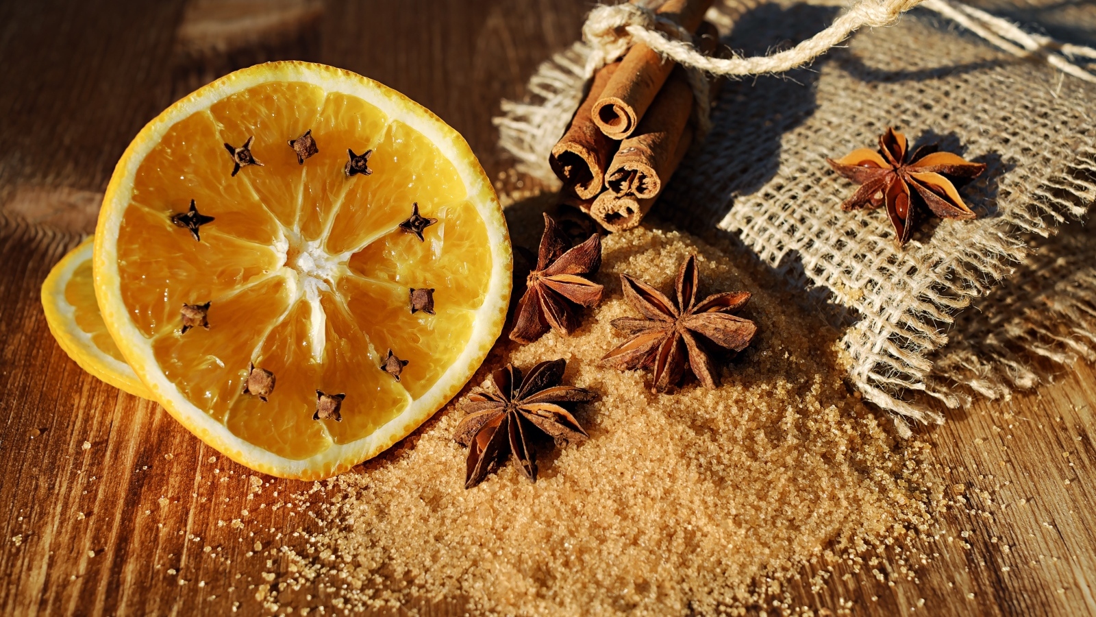 Апельсин с гвоздикой на столе с сахаром, корицей и бадьяном