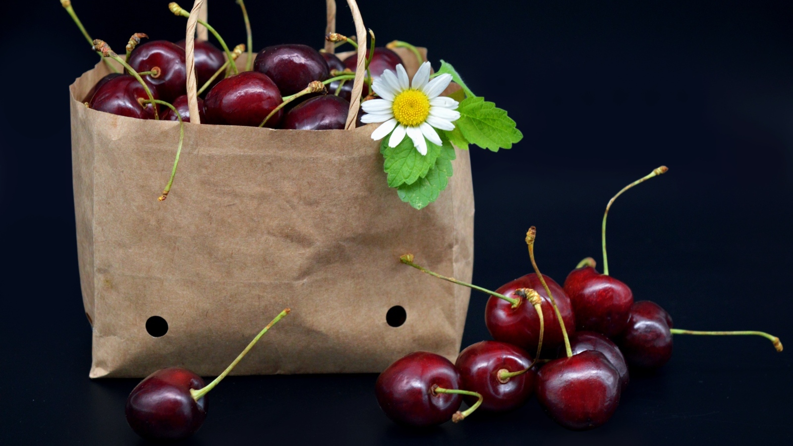 Бумажный пакет с ягодами черешни на черном фоне