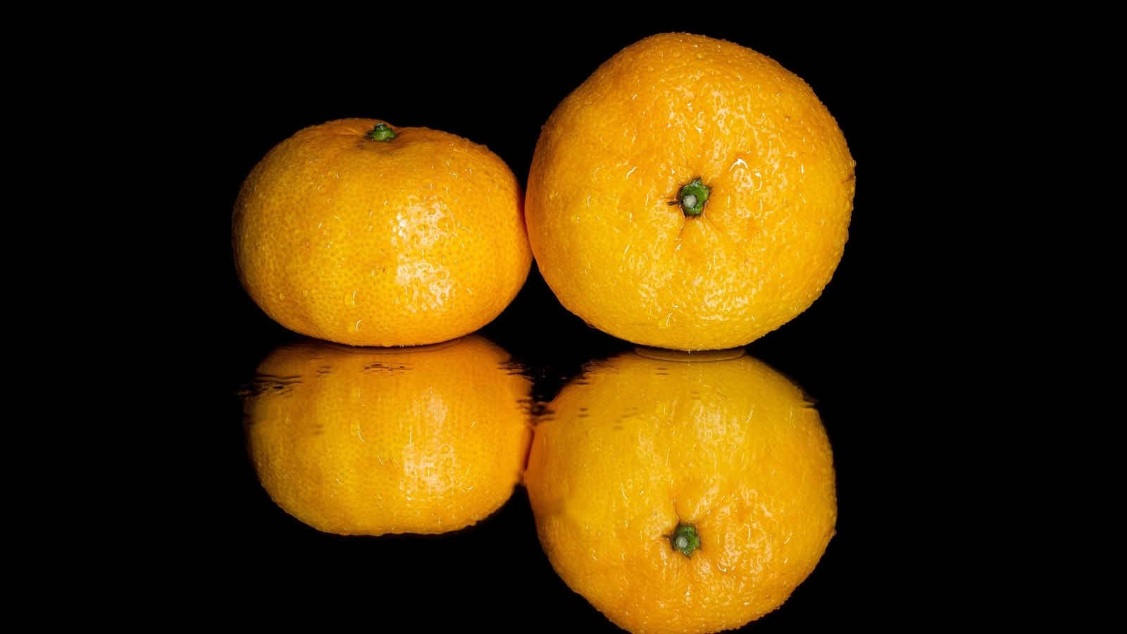 Два мандарина на черной зеркальной поверхности 