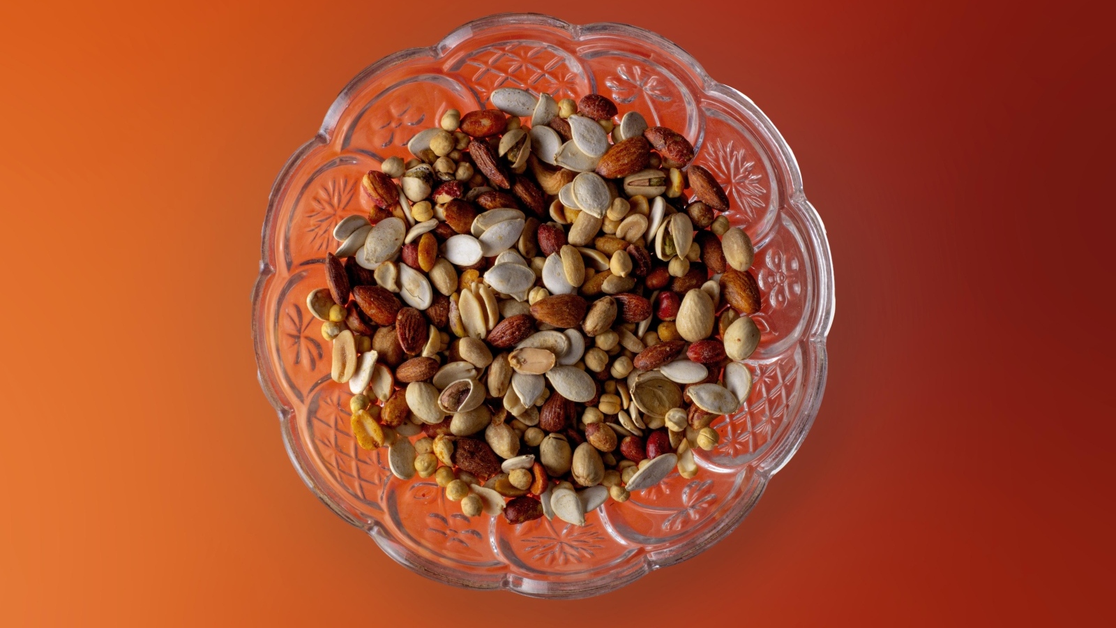 Разные орехи в стеклянной посуде на оранжевом фоне