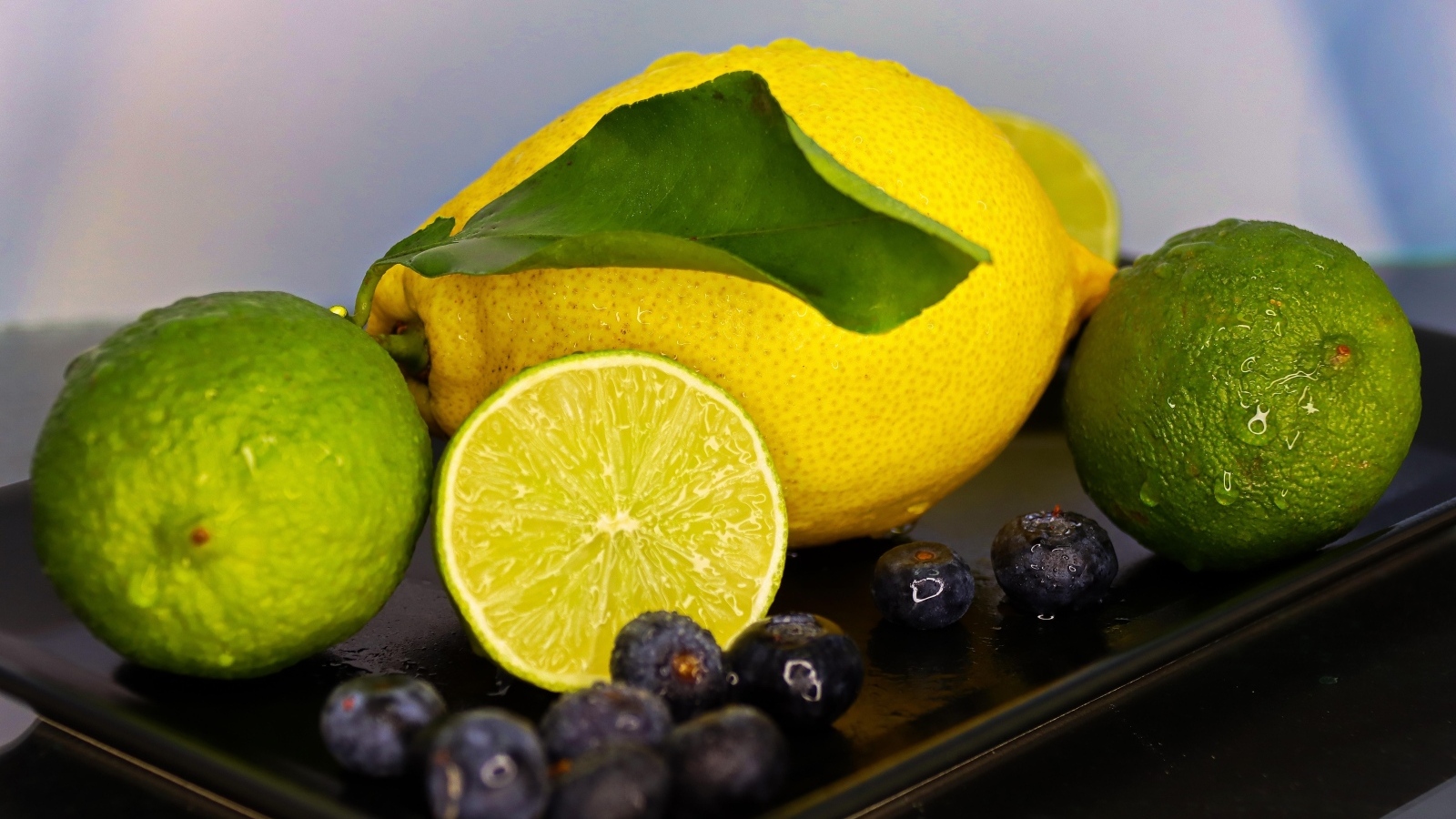 Желтый лимон на тарелке с лаймом и ягодами черники 