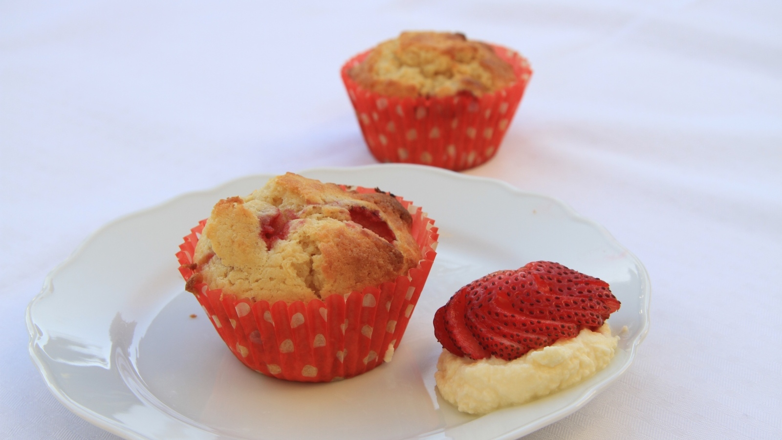 Кекс на большой белой  тарелке с кремом и клубникой