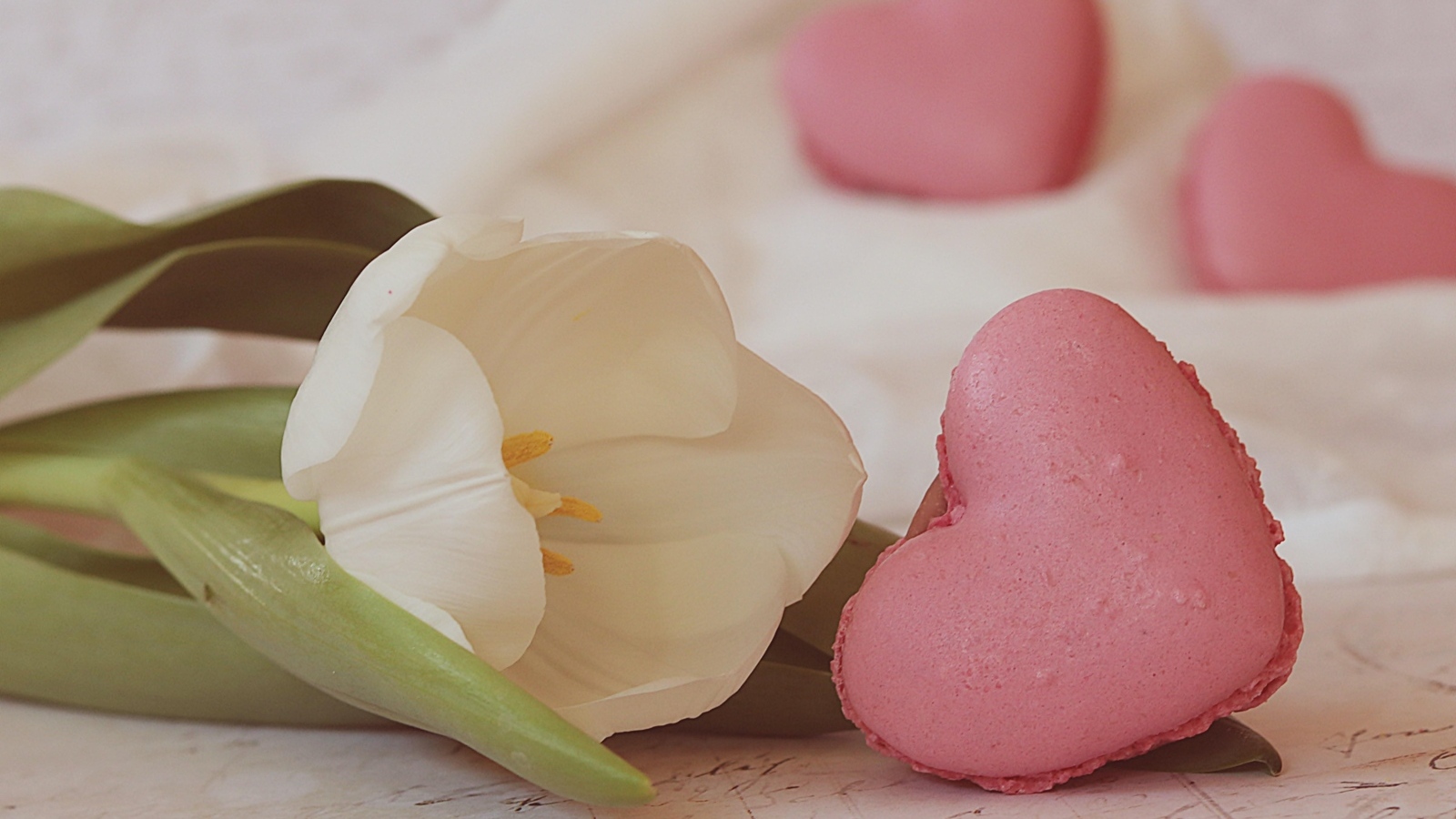 Десерт макарун в форме сердца на столе с тюльпаном