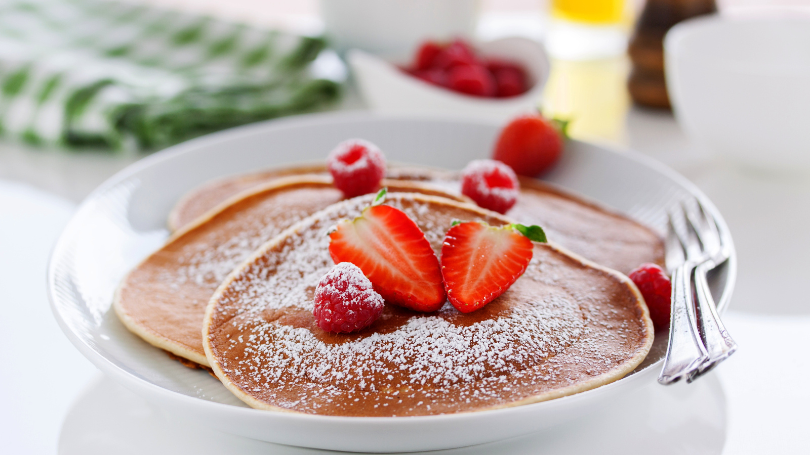Оладьи на тарелке с сахарной пудрой и ягодами клубники
