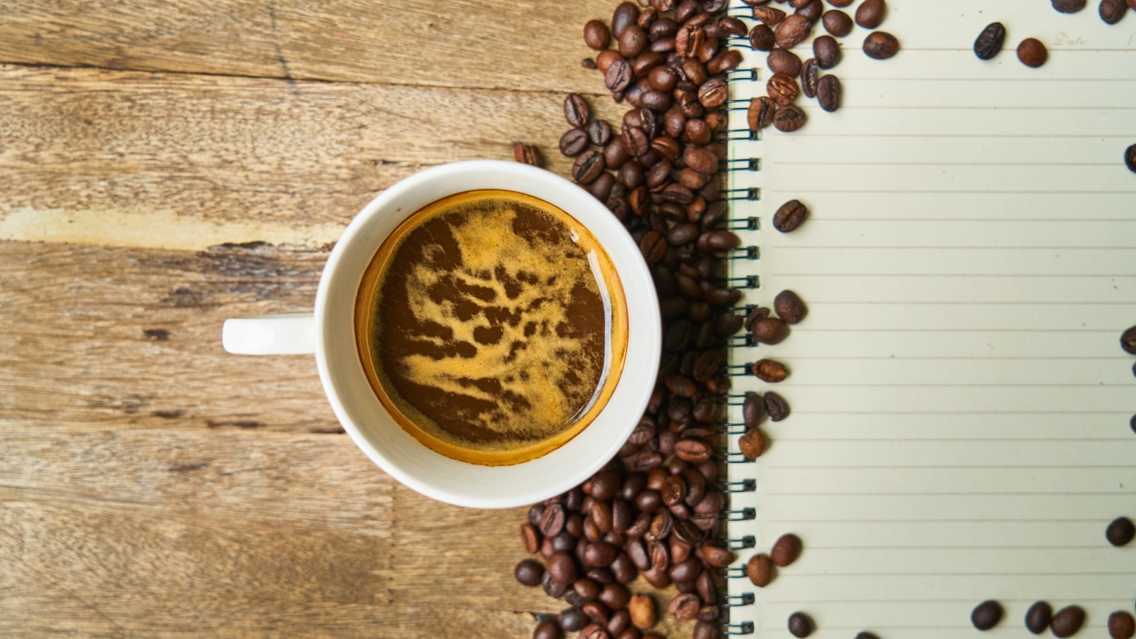 Чашка кофе на столе с зернами и блокнотом