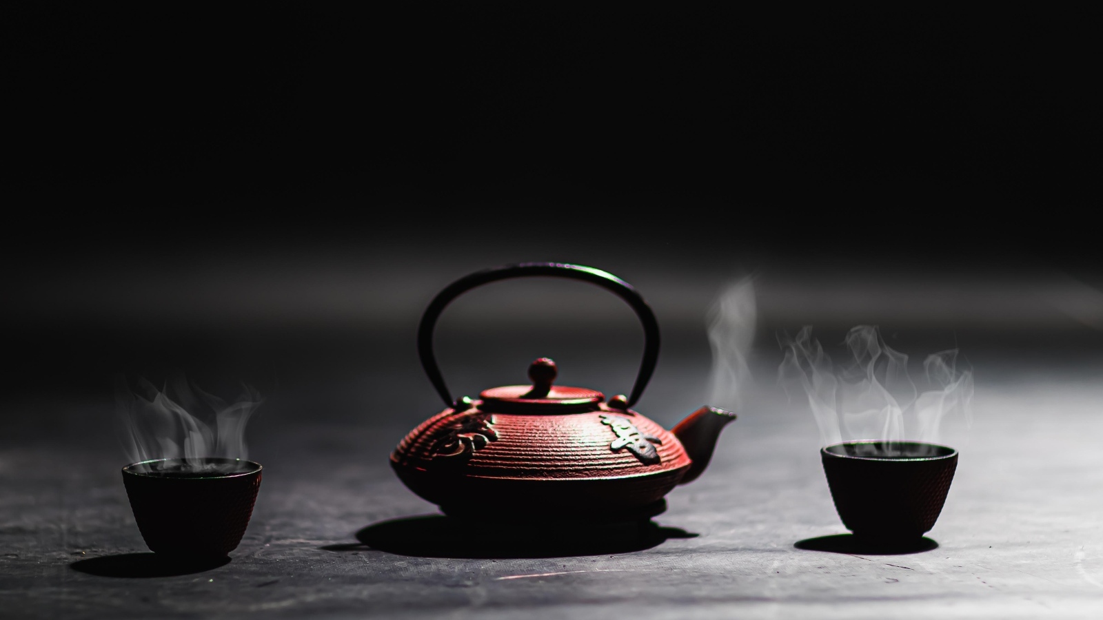 Чайник с горячим чаем на черном фоне