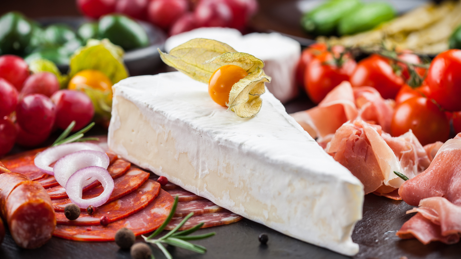 Кусок сыра на столе с овощами и колбасой