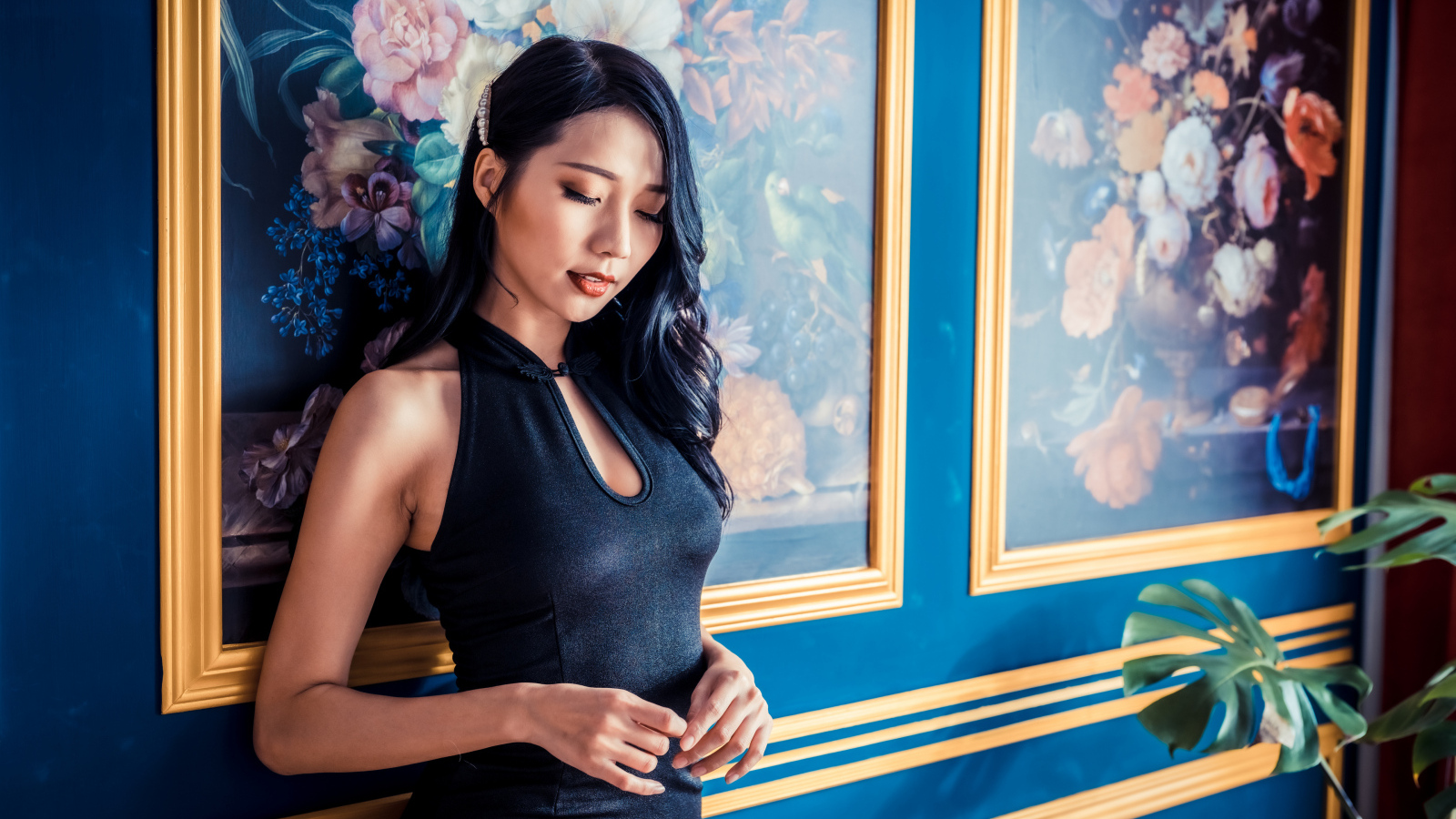 Красивая девушка азиатка в черном платье стоит у картины 