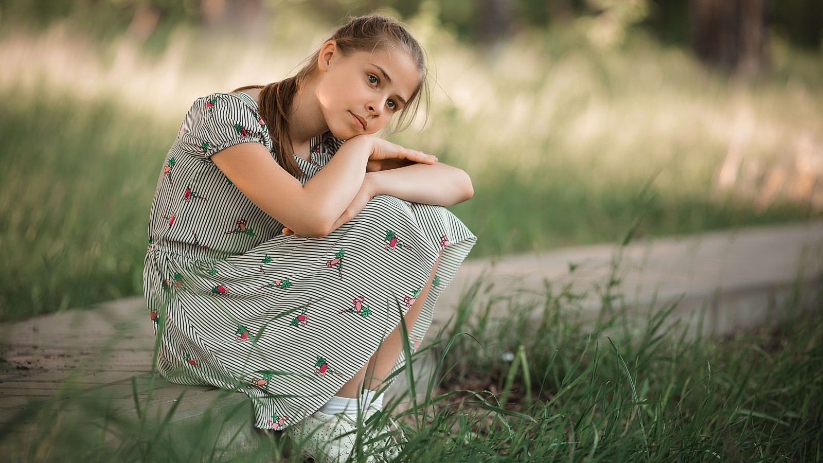 Девушка в платье сидит у зеленой травы
