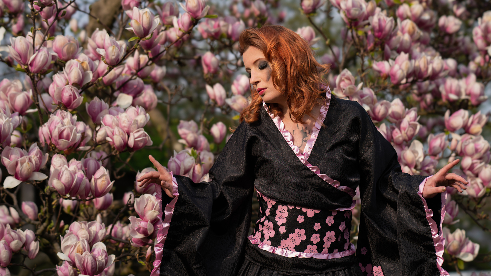 Девушка в кимоно стоит у куста с цветами магнолии