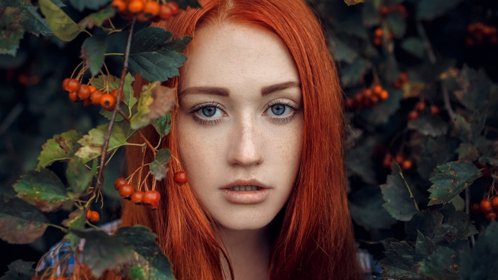 Рыжеволосая девушка стоит у куста с боярышником