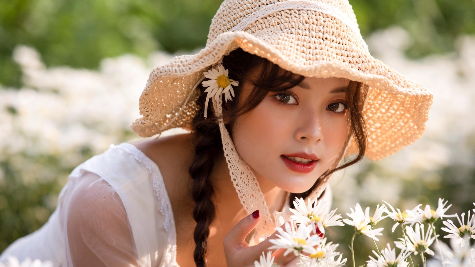 Девушка азиатка в шляпке на поле с ромашками