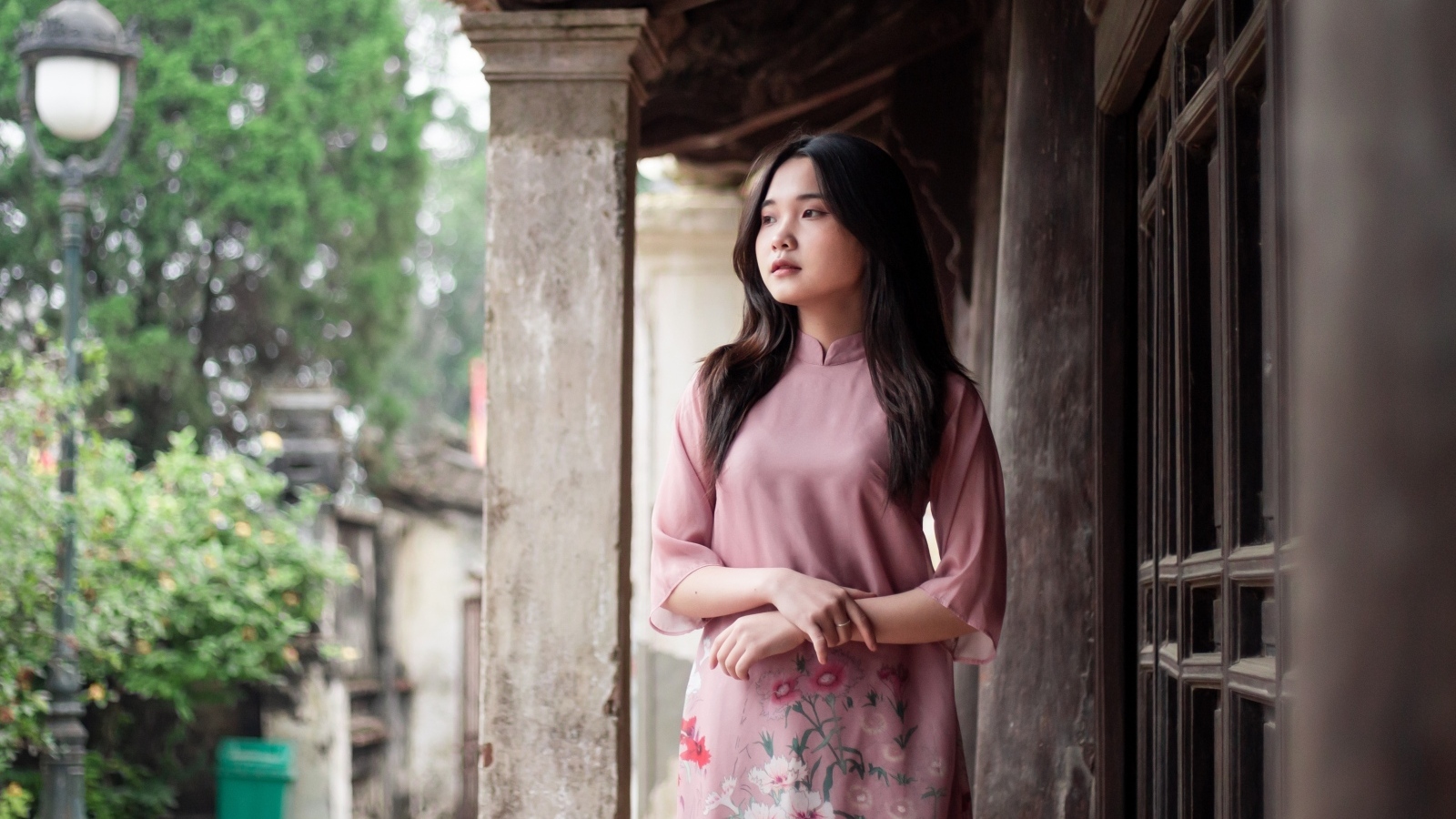 Девушка азиатка в розовом платье стоит у дома