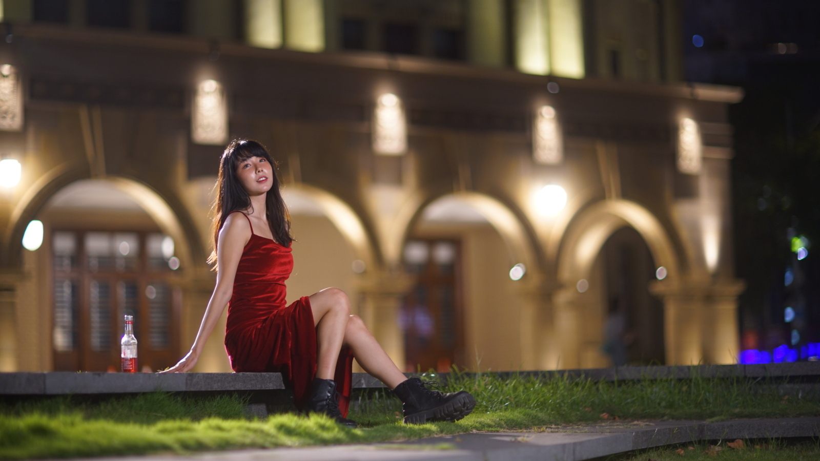 Азиатка в длинном красном платье сидит на ступенях