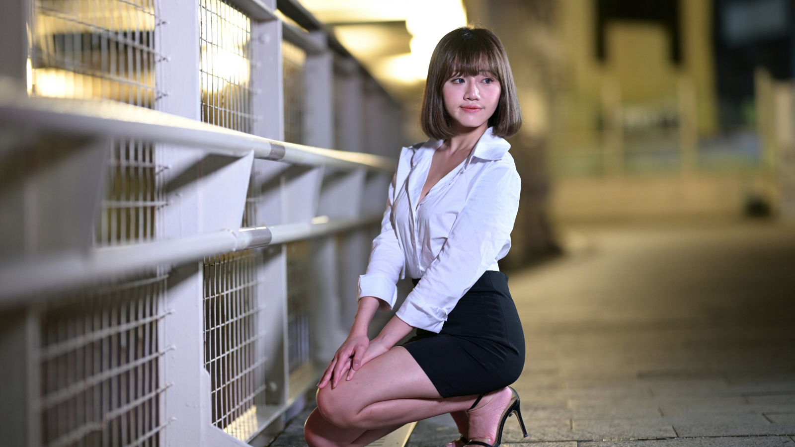 Азиатка в белой блузке и черной юбке сидит на корточках