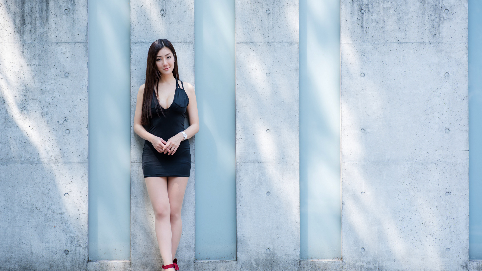 Красивая азиатка в коротком платье стоит у стены