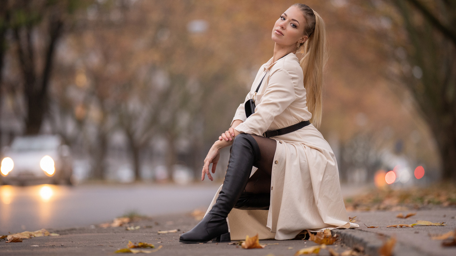 Девушка блондинка сидит в пальто в парке