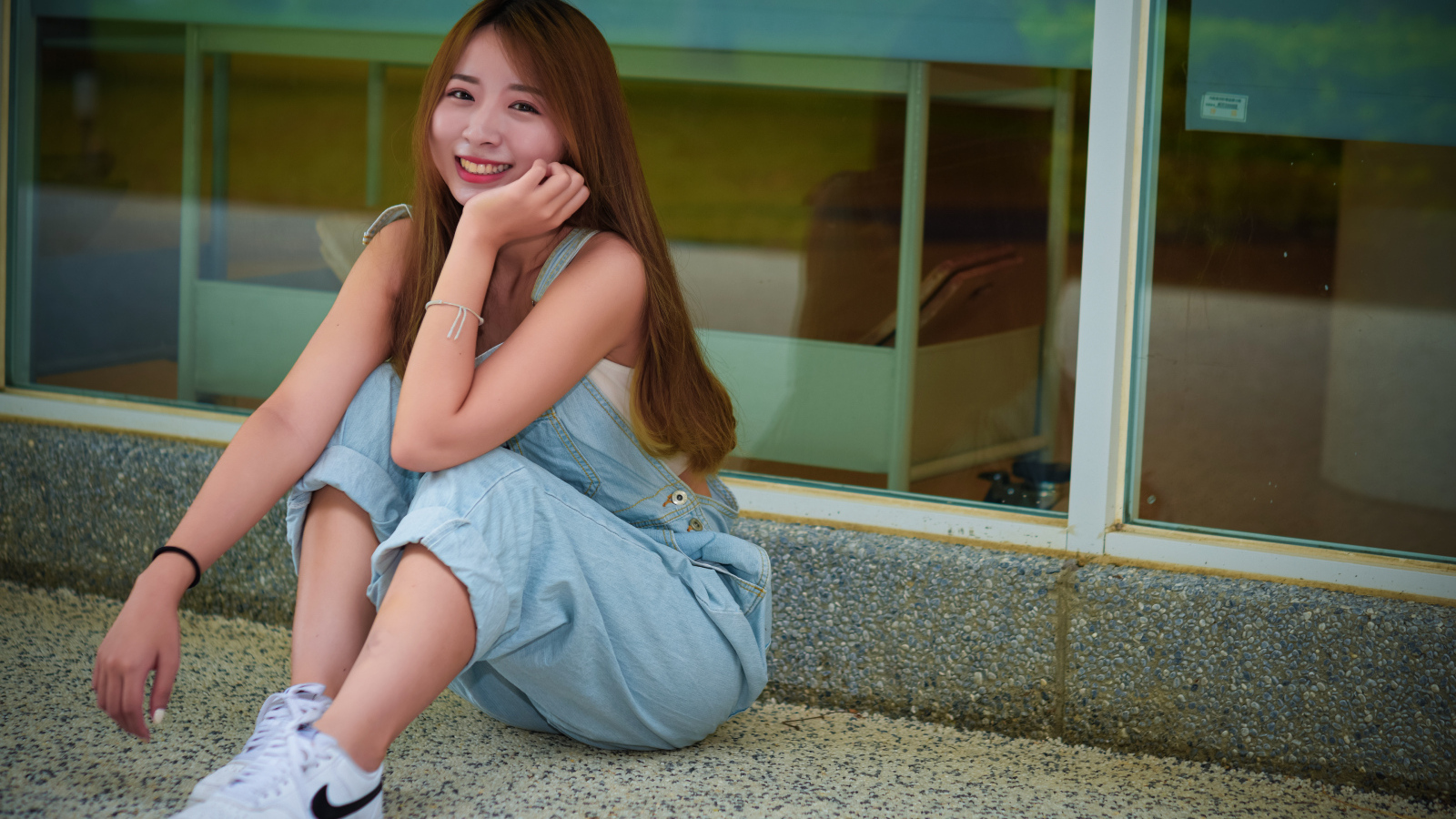 Девушка в джинсовом комбинезоне сидит на полу