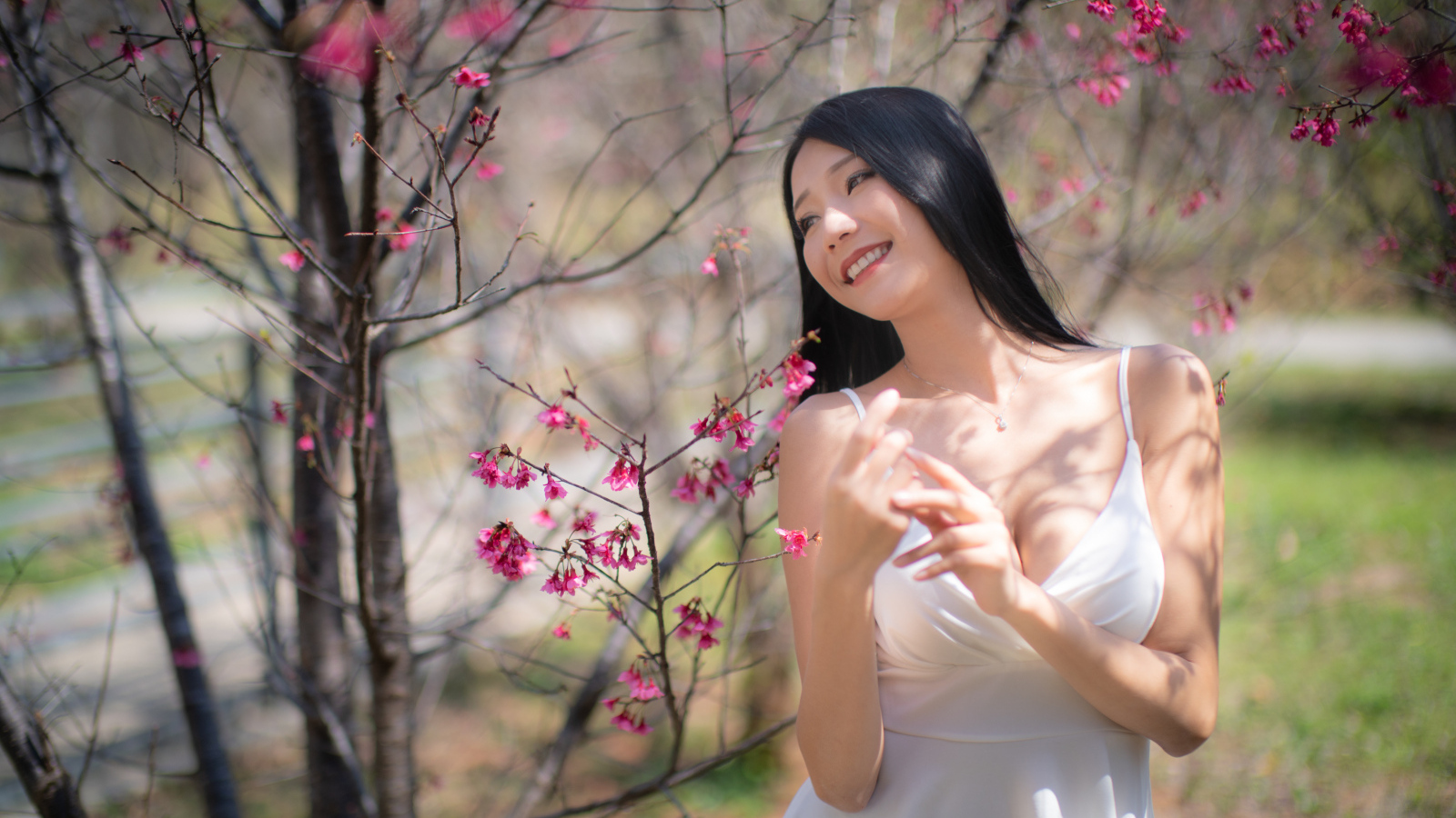 Улыбающаяся девушка в белом платье у дерева с цветами