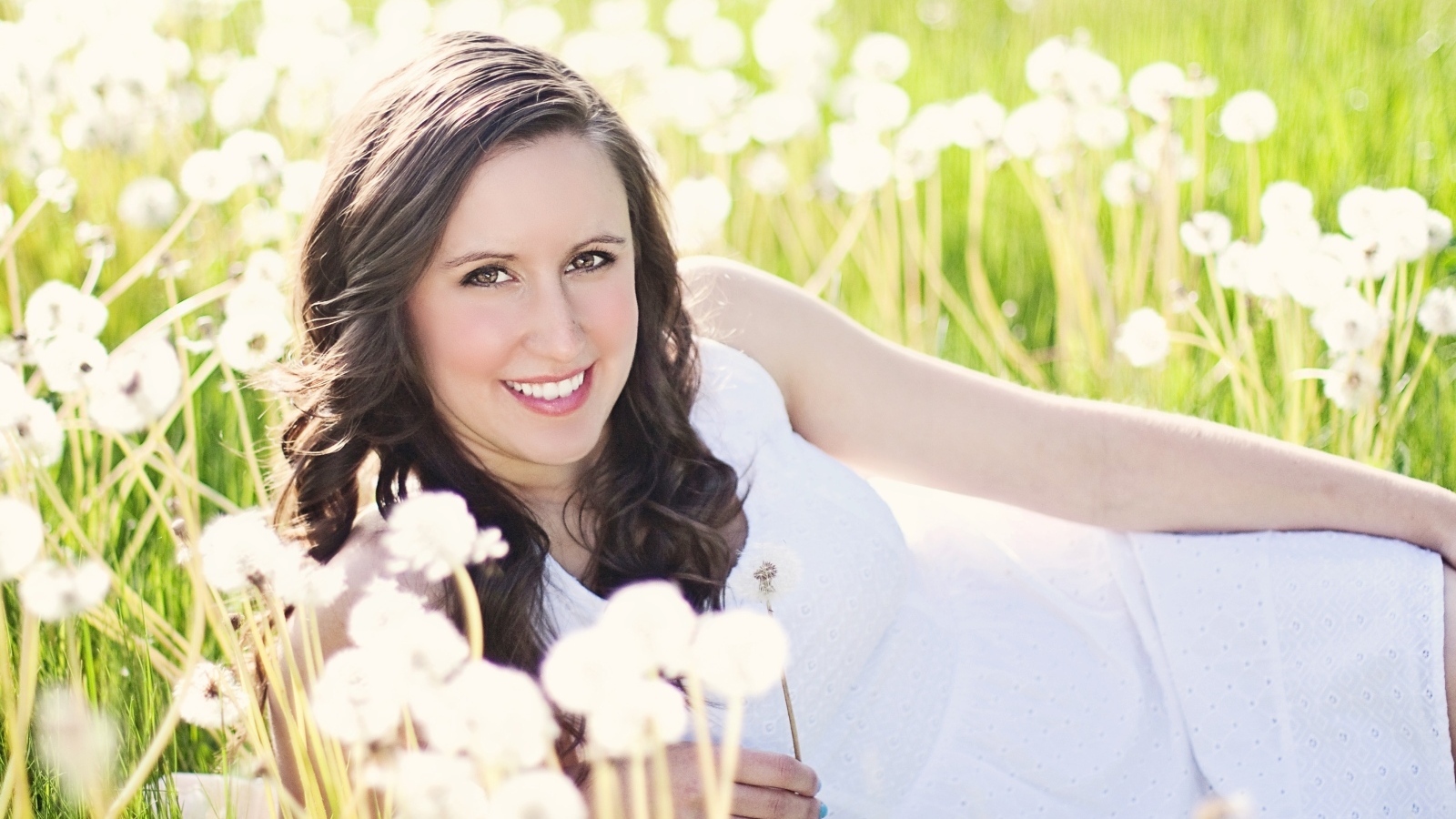 Улыбающаяся девушка лежит на поле с одуванчиками