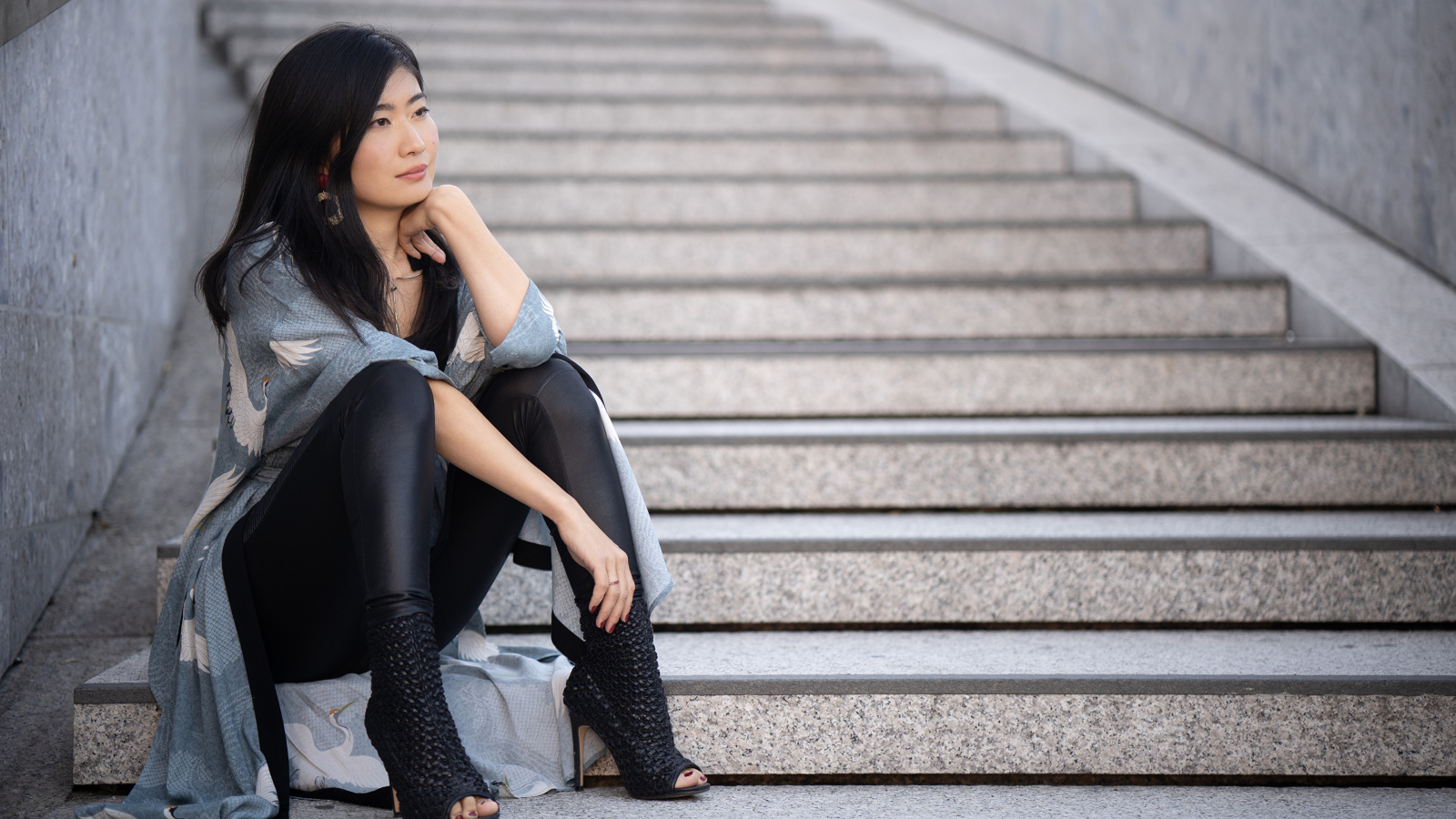 Задумчивая девушка азиатка сидит на ступеньках