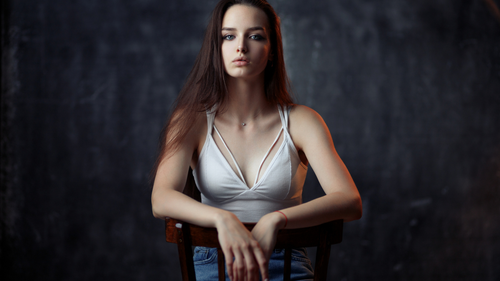 Молодая длинноволосая девушка сидит на деревянном стуле