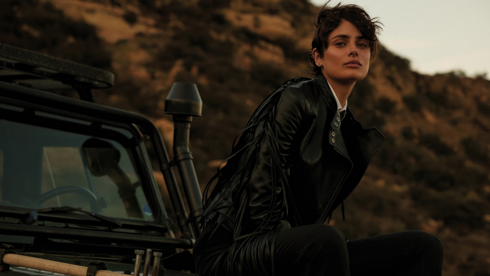 Модель Тейлор Хилл в черной куртке сидит на машине