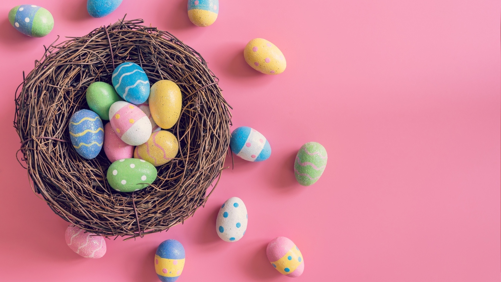 Гнездо с разноцветными яйцами на розовом фоне на Пасху