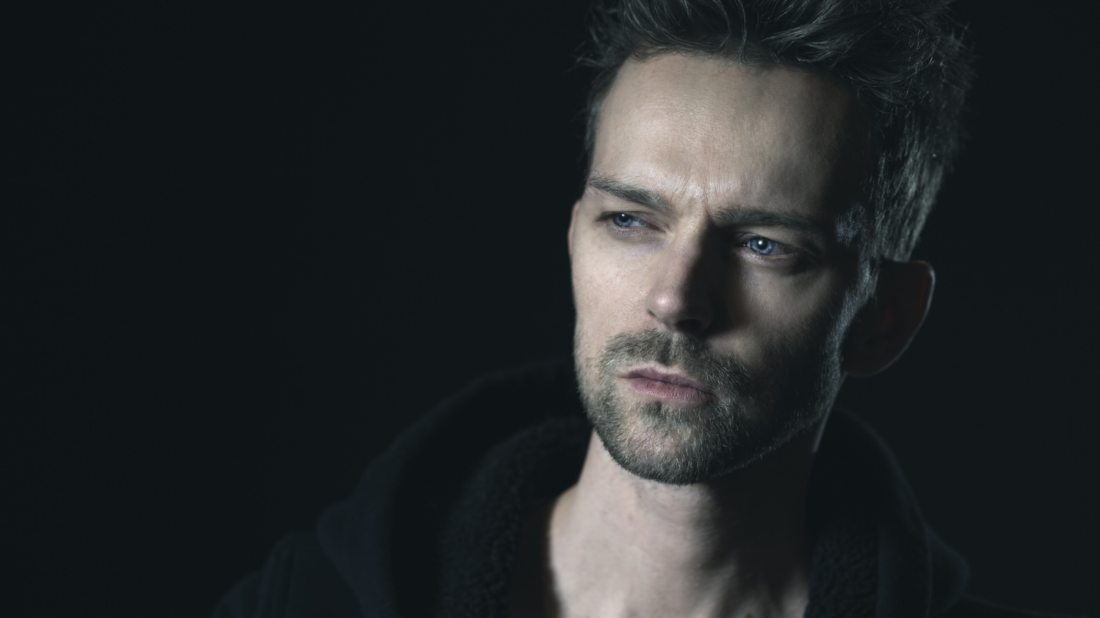 Серьезный голубоглазый мужчина на черном фоне