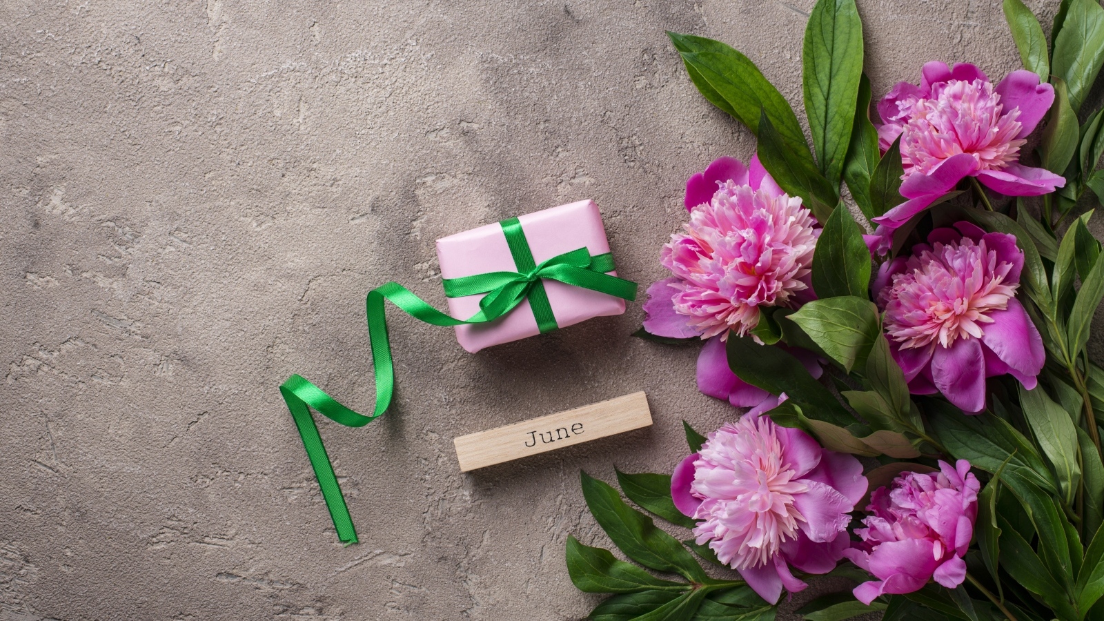 Букет розовых пионов с подарком на сером столе