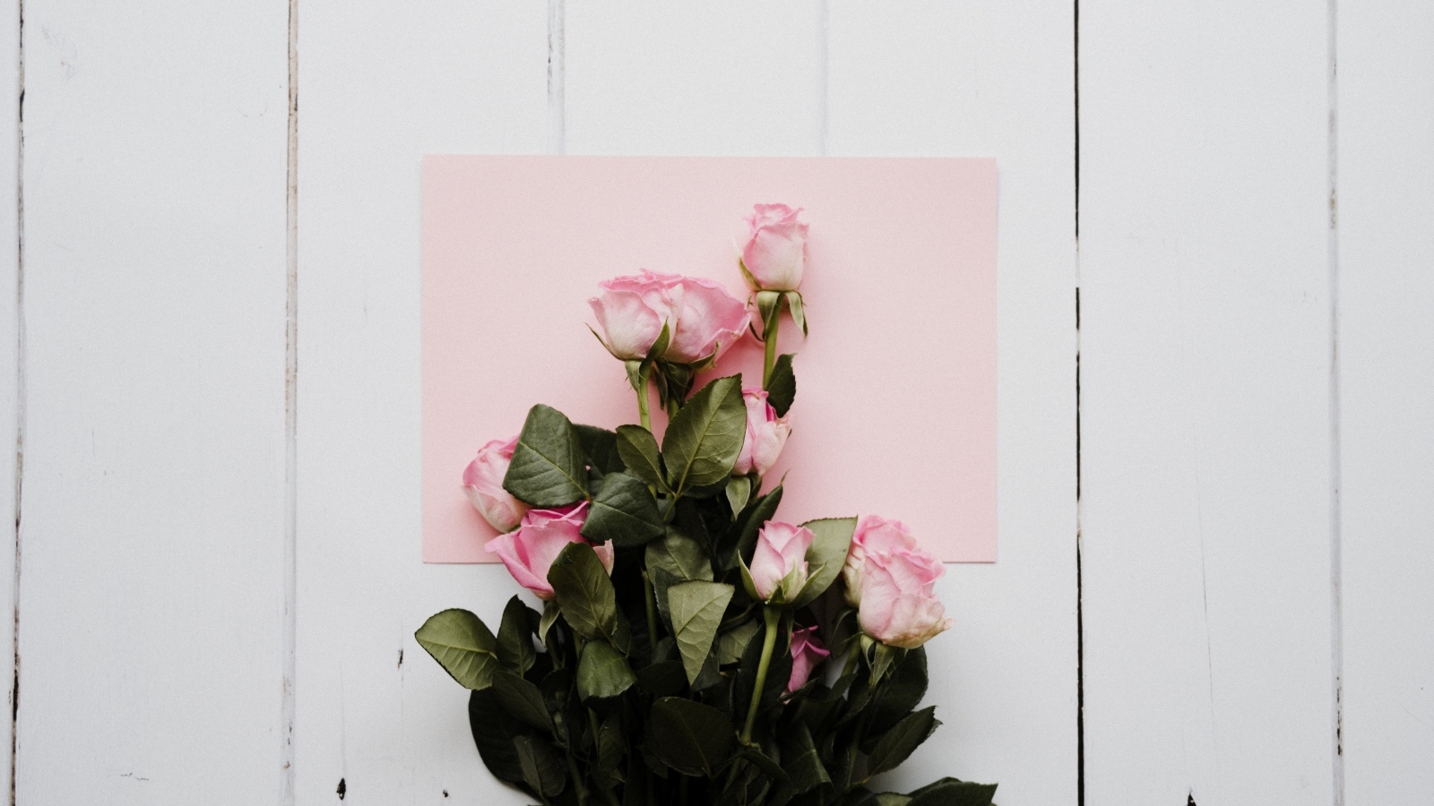 Букет роз с розовым листом бумаги на столе