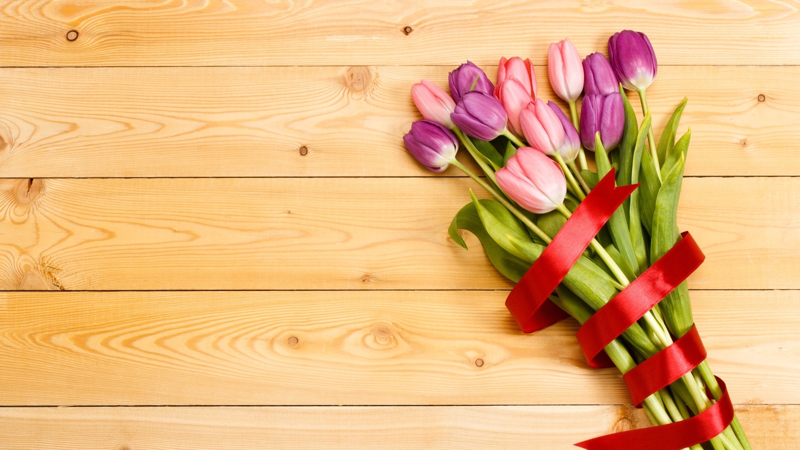 Большой букет тюльпанов с красной лентой на деревянном фоне