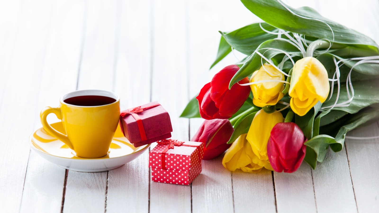 Желтая чашка кофе на столе с подарками и букетом тюльпанов
