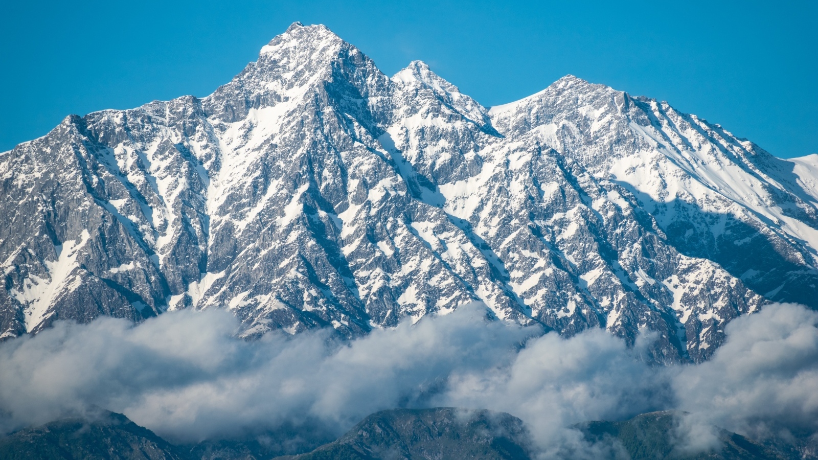 Высокие заснеженные горы в тумане под голубым небом