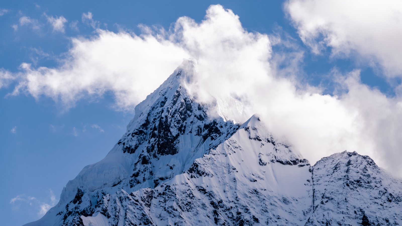 Острая заснеженная вершина горы в белых облаках