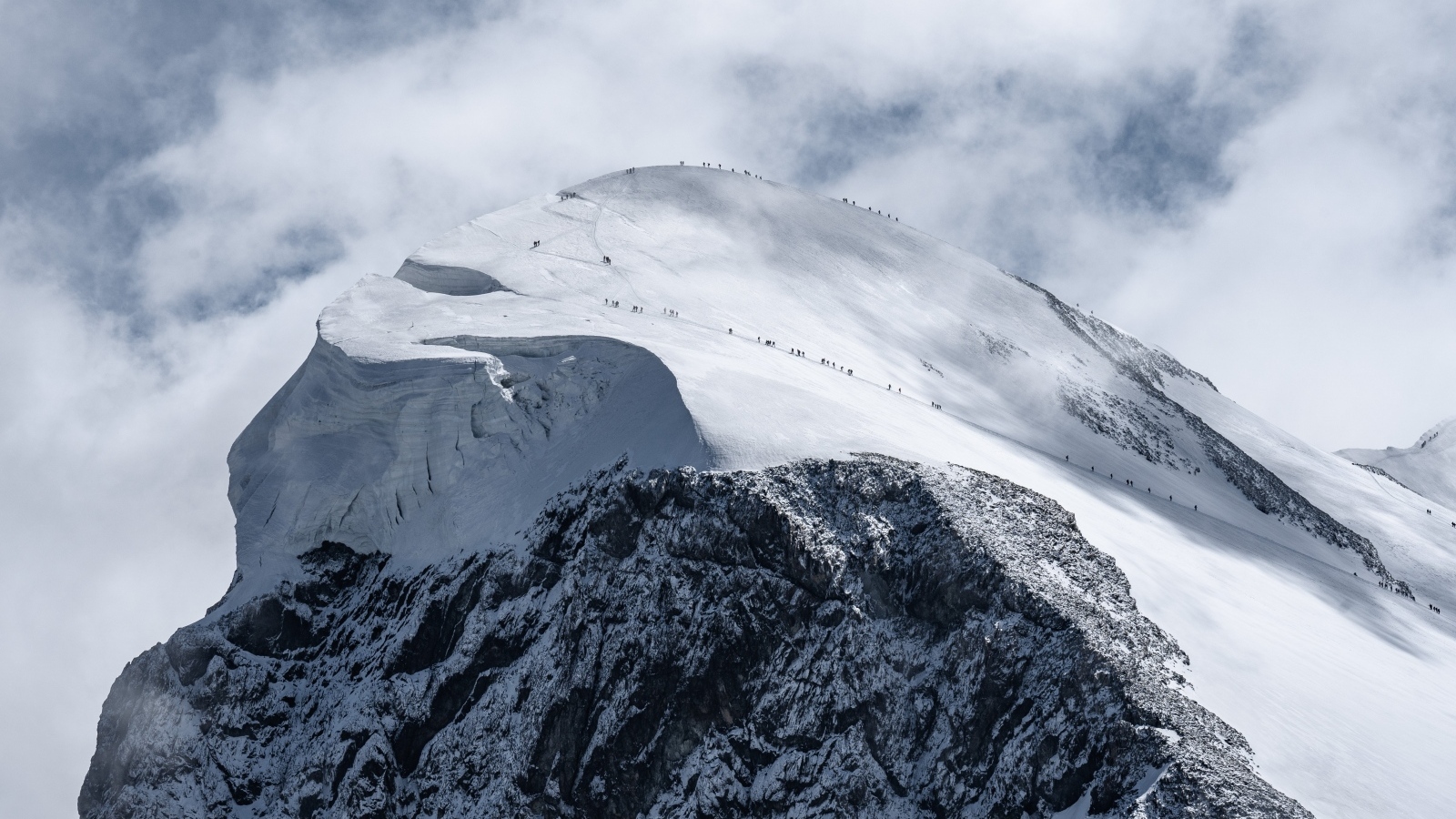 Вид на заснеженную вершину горы под белыми облаками