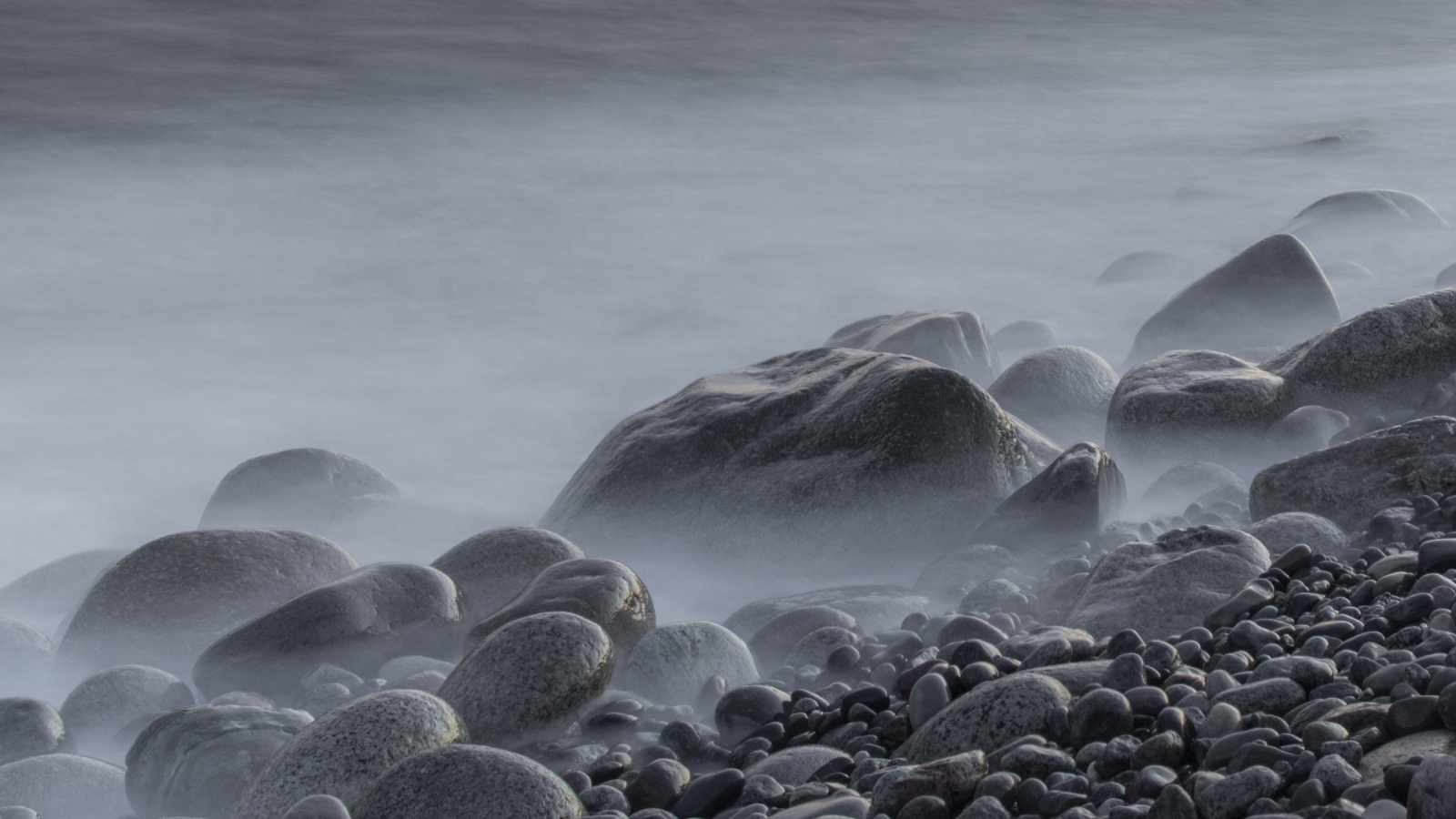 Большие черные камни на берегу моря в тумане