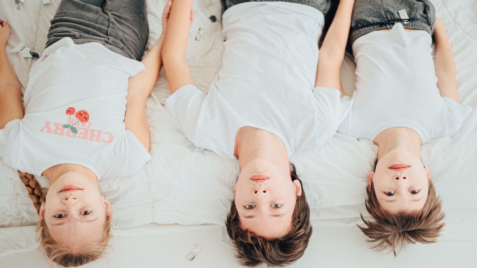 Дети в белых футболках лежат на кровати