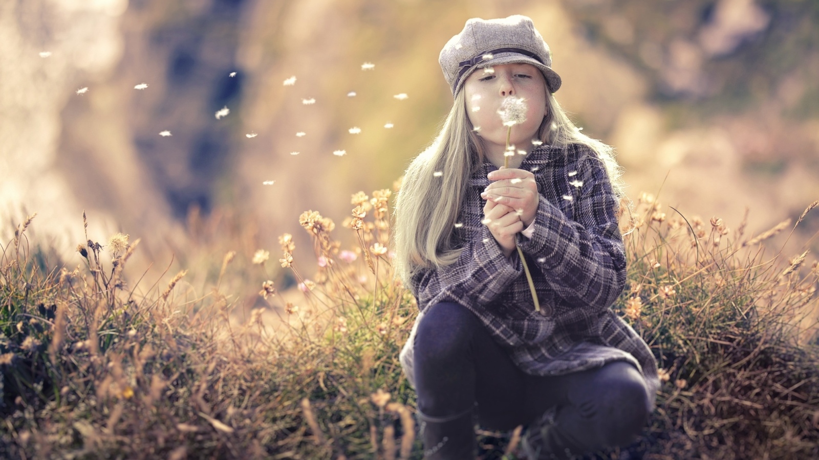 Девочка в кепке сдувает одуванчик