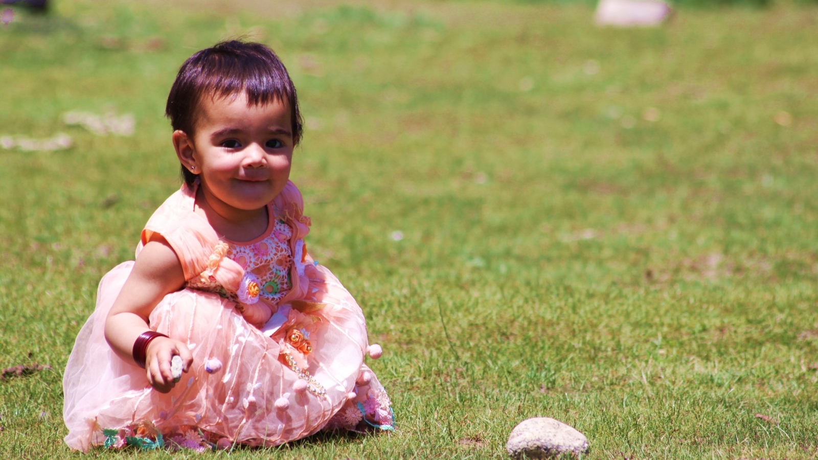 Девочка в розовом платье играет на зеленой траве