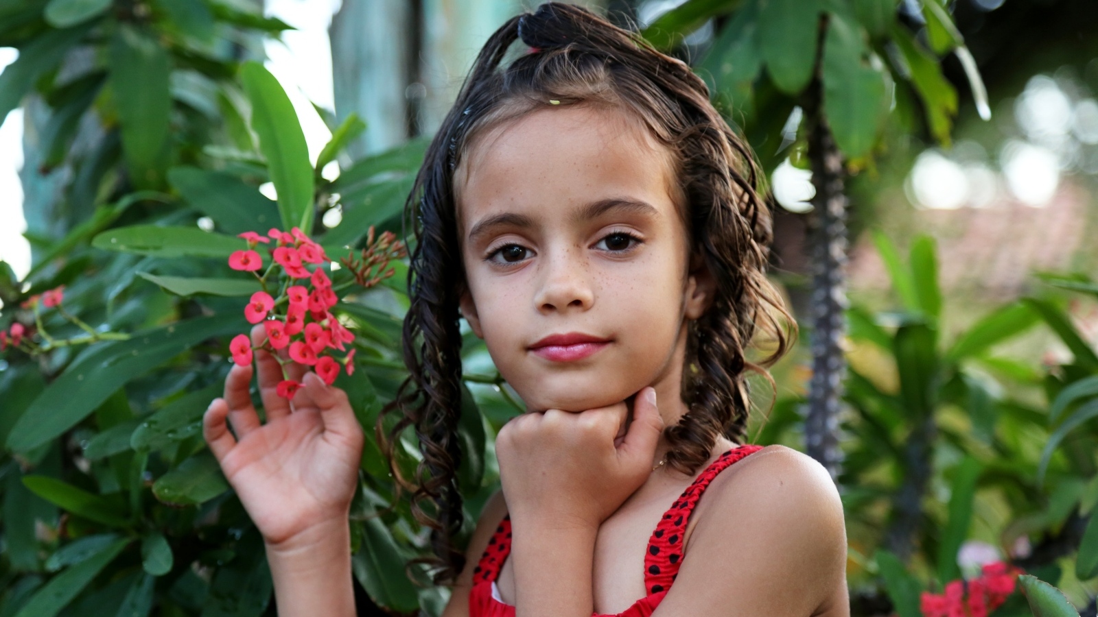 Девочка стоит у ветки с красными цветами